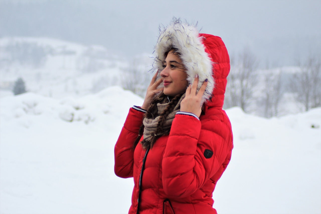 "Woman in a red winter coat with faux fur hood standing in a snowy landscape."